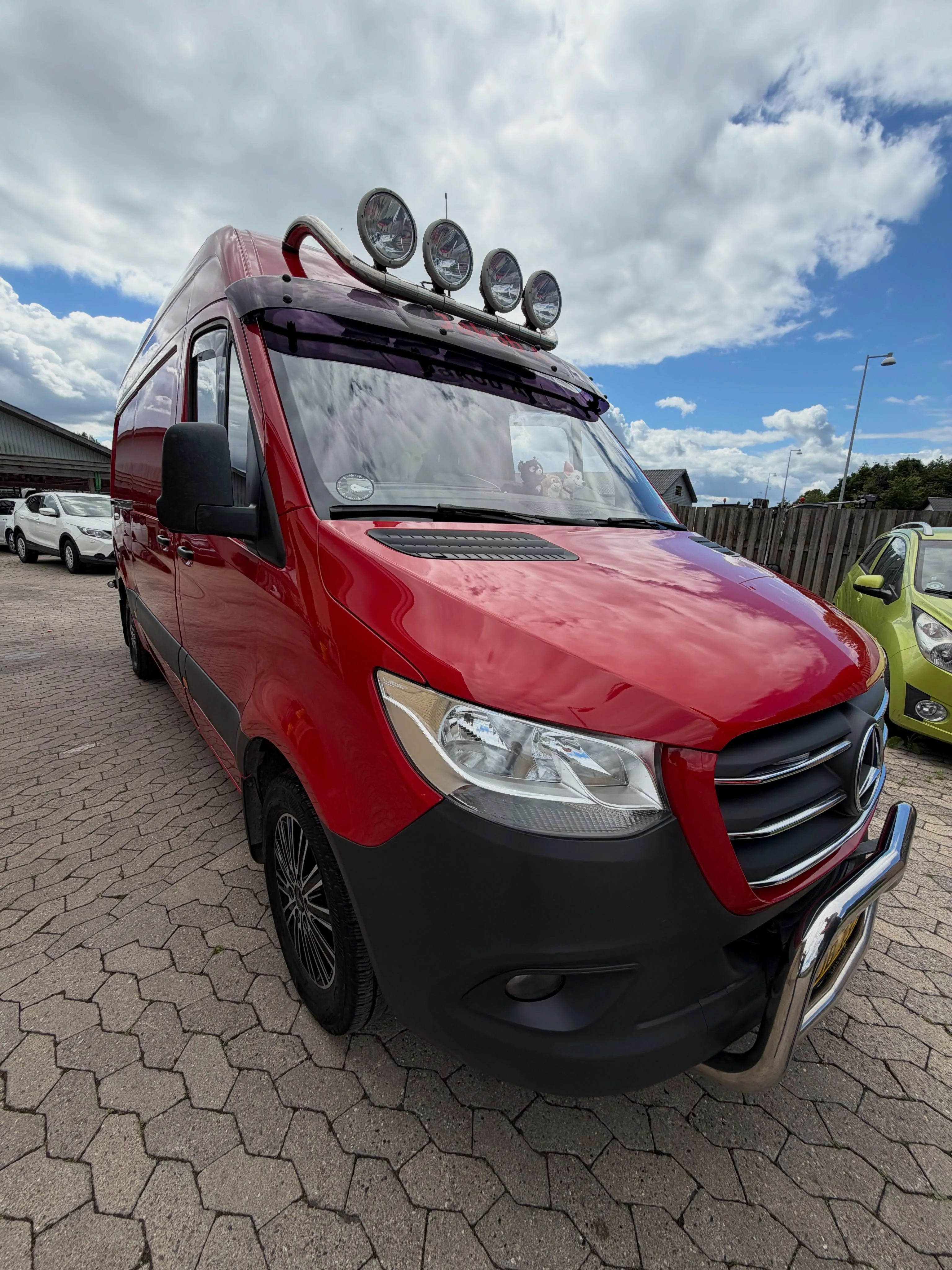 Rød Mercedes Sprinter set forfra med ekstralys på tag, fotograferet udenfor på brosten.