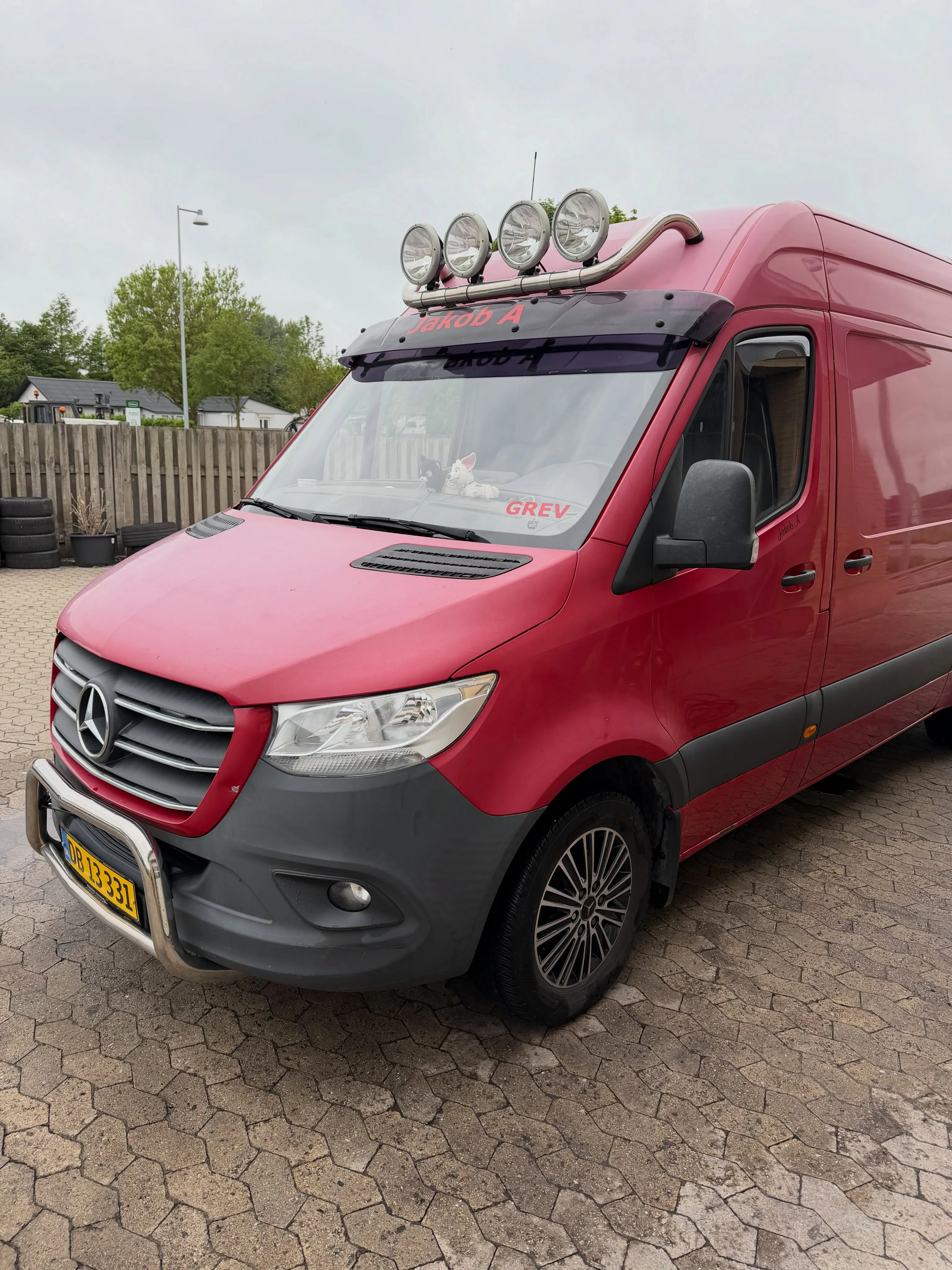 Rød Mercedes-Benz Sprinter varevogn set forfra i vinkel, med ekstralys på tag og forkofanger.
